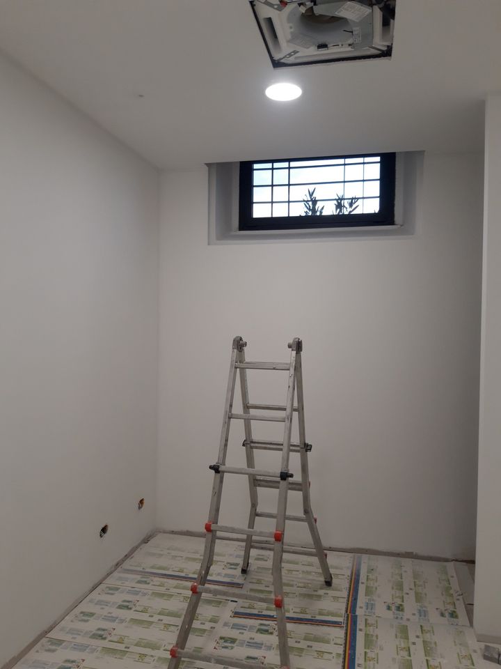 Stanza tinteggiata di bianco con finestra alta, scala e pavimento ancora protetto
